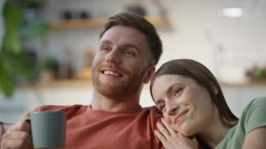 Kanepede dinlenen ve yakınlaşmanın tadını çıkaran bir çift. Gülümseyen koca elinde kahve fincanıyla sevgili karısıyla konuşuyor. Evli çiftler birbirlerine sarılıp romantik ev anlarını paylaşıyorlar..