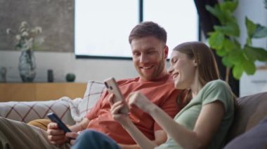 Gülen eşler oturma odasındaki kanepede dinlenen telefonları izliyorlar. Mutlu kadın cep telefonlarını karıştırıyor. Kanepede komik videolar çekiyor. Rahat evli çift akıllı telefonlardan haberleri tartışıyor..