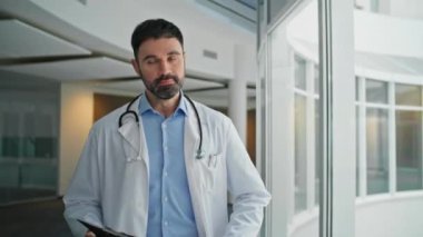 Ciddi bir terapist teşhis panosuna bakıyor. Yakın plan tedaviden dolayı üzgün doktor koridorunda yürüyor. Odaklanmış sağlık uzmanı hastanedeki hasta çizelgesini kontrol ediyor. Beyaz önlüklü düşünceli adam.