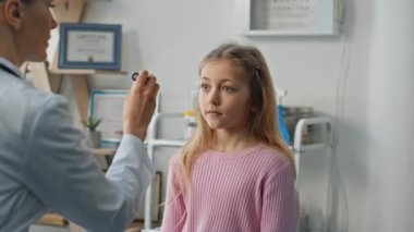 Sağlık kontrolü sırasında el feneri kullanan bir çocuk doktoru. Yakın plan sarışın kız özel klinikte çocuk doktorunu ziyaret ediyor. Sağlık uzmanı nörolog refleksleri test ediyor..