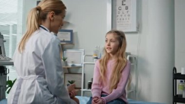 Klinikteki çocuk doktoru randevusu yakın planda. Gülümseyen kadın hastane odasında sevimli bir hastaya danışıyor. Profesyonel sağlık çalışanı pratisyenini dinleyen güzel bir çocuk. Çocuk bakımı ilaçları