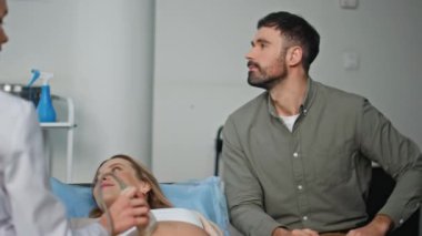 Modern klinikte ultrasonu ziyaret eden mutlu çift. Karın taraması yapan bir doktor ultrasonda ultrasona girdi. Neşeli adam baba, karısını destekliyor ve hamilelik konusunda heyecanlı. Gülümseyen aileler bir arada
