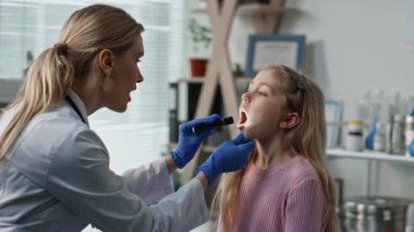 Çocuk doktoru el feneriyle kızın boğazını inceliyor. Profesyonel doktor pediatri kliniğinde grip sonrası anjini kontrol ediyor. Tatlı çocuk terapisti randevusu. Tıbbi kontrol kavramı