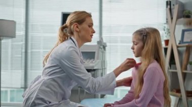 Sağlık çalışanı muayene odasında çocuk sağlığını kontrol ediyor. Endişeli kadın doktor vücut ısısını ölçüyor. Özel klinikte üzgün bir çocukla konuşuyor. Beyaz önlüklü genel terapist.