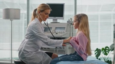 Kadın dinleme çocuk steteskobu muayene odasında. Beyaz önlüklü, doktorla konuşan tatlı bir çocuk. Dost canlısı çocuk doktoru, özel klinikte sağlık kontrolü sırasında tedavi tavsiyesi verdi