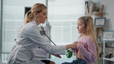 Çocuk doktoru sağlık kontrolü sırasında steteskop kullanıyor. Tatlı çocuk ziyaret kliniği. Odaklanmış sağlık çalışanı, küçük bir hastaya teşhis konusunda vücut danışmanlığı yapıyor. Pediyatri uzmanı hasta kız konuşuyor.