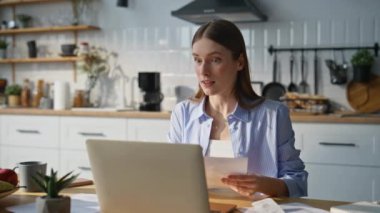 Ev mutfağındaki bilgisayarın görüntülü sohbetinde olumlu bir öğretmen konuşuyor. Gülümseyen iş kadını, çevrimiçi konferansta kağıtları analiz ediyor. Bağımsız çalışan internet toplantısının tadını çıkarsın.