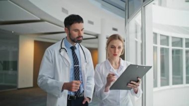 Doktor hasta çizelgesi hakkında konuşuyor. Tıp ekibi hastanede yürüyor ve modern klinikte tedaviyi tartışıyorlar. Paltolarla koridora çıkan kendine güvenen sağlık görevlileri. Personel işbirliği