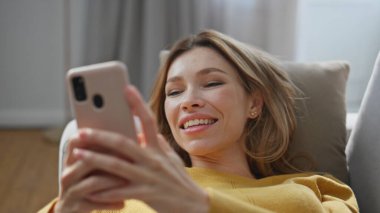 Mutlu bayan kanepeye uzanmış cep telefonunu kapatıyor. Evde akıllı telefon kullanarak mesaj yazan kaygısız bir kadın. Neşeli, rahat kız hafta sonunun tadını çıkarıyor yalnız başına. İnsan yaşam tarzı 