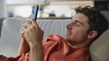 Mutlu adam kanepeye uzanıp cep telefonuna mesaj yolluyor. Gülümseyen kaygısız adam evde akıllı telefon kullanarak mesaj yazıyor. Neşeli gevşemiş hipster hafta sonunun tadını çıkarıyor hafta sonları yalnız takılıyor.