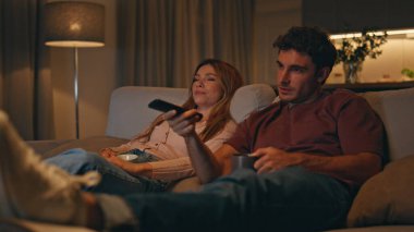 Gülümseyen eşler akşam geç saatlerde oturma odasında oturmuş televizyon seyrediyorlar. Mutlu evli çiftler kanalı değiştirip gece evlerinde eğleniyorlar. Aile eğlencesi hafta sonu konsepti. 