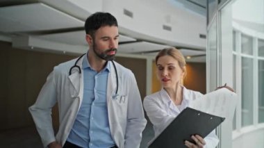 Koridordaki sağlık hemşiresine yakın çekim. Sağlık çalışanları evlerinde dokümanları inceliyor. Odaklanmış tıbbi ekip ameliyattan önce hasta dosyasını tartışmaya gidiyor. Beyaz önlüklü doktorlar.