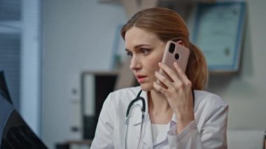 Doktor, akıllı telefondan kötü haberleri iletiyor. Yakın plan endişeli kadın röntgen sonuçlarını analiz ederken tıbbi muayenehanede görünüyor. Stresli radyoloji uzmanı hastalarıyla cep telefonu konuşarak şakakları ovalıyor.