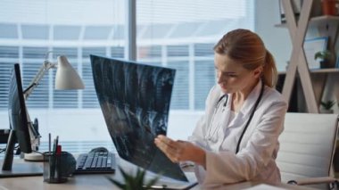 Muayenehanede röntgen analizi yapan düşünceli bir doktor. Yakından bakan kadın, Buro 'da hasta teşhisi üzerinde çalışıyor. Profesyonel sağlık çalışanı tedavi düşünüyor Klinikte radyografiyi kontrol ediyor.