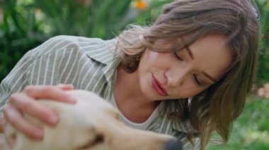 Güneşli yeşil doğada gülümseyen ve köpeği okşayan bir kadın. Mutlu kürklü golden retriever sahibi park çimlerini seviyor. Sevgi dolu bayan, sağlıklı kürklü hayvanları okşuyor. Hayvan dostluğu kavramı.