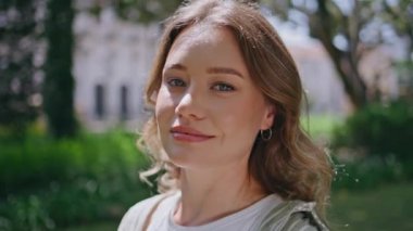 Parkta poz veren çekici bir model çevresi canlı yeşilliklerle çevrili. Güneşli doğada durup tasasız yaz haftasonunun tadını çıkaran güzel genç bir kadının portresi. Rahatlamış bayan gülümseyen kameraya bakıyor..