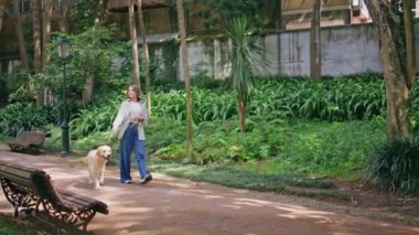 Tasasız kadın, yapraklı patikada yürüyen bir hayvan. Kentsel yeşil alanda Golden Retriever 'la gezen rahat bir kadın. Kendine güveni tam bir köpek sahibi. Etrafı yaz yeşillikleriyle çevrili..