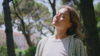 Kaygısız bir kız güneş ışığında güneşleniyor. Gözlerini kapıyor. Yüzünde doğal bir ifade var. Yaz güneşinin tadını çıkaran genç ve güzel bir kadın yeşil bahçede tek başına dinleniyor. Sunny Park sükunet konsepti.