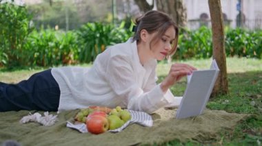 Sunny Park 'ta piknik üzerine kitap okuyan bir kadın. Sayfaları çeviren güzel bir kız barışçıl doğada kitap uzanırken eğleniyor. Sakin esmer, meyva ve edebiyatla çayırda dinleniyor..