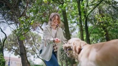 Yeşil güneşli parkta evcil hayvancılık oynayan gülen kız. Mutlu aktif kadın sağlıklı Golden Retriever ile eğleniyor. Neşeli köpek, gülümseyen kadın sahibinden sopa alıyor. Arkadaşlık kavramı