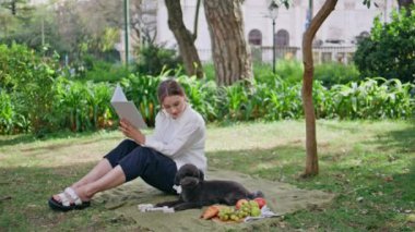 Tüylü sevimli köpekle yaz pikniğinde dertsiz tasasız romantik roman okuyan kadın. Mutlu kadın siyah kanişiyle battaniyenin üzerinde oturan ilginç kitaptan zevk alıyor. Rahat kız hafta sonunu sevimli bir evcil hayvanla geçiriyor..