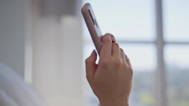 Modern yatak odasında akıllı telefon tutan kadın elleri. Gülümseyen kadın cep telefonu sosyal medyasında rahat bir yatakta yatıyor. Çekici kız gülerek sabah erkenden yastıkta cep telefonu mesajı okuyor..