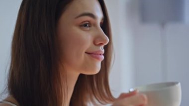 Gülümseyen kadın, sakin bir sabahta kahve tadıyor. Sıcak ev ortamında sıcak kapuçino içen mutlu esmer portresi. Nazik ifadeli huzurlu genç kız evde içkinin tadını çıkarıyor.