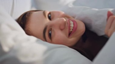 Kapalı yerde, battaniyenin altında, rahat bir yatakta uzanmış mutlu bir şekilde yakın çekim yapıyor. Gülümseyen kadın rahat beyaz yatak odası kamerasında dinleniyor. Neşeli esmer, rahat yatak odasında evcil sabahın tadını çıkarıyor..
