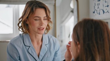 Modern yatak odasında pozitif anne kızı konuşuyor. Önemseyen bir kadın, küçük bir çocukla iletişim kurup hafta sonunun tadını çıkarıyor. Pijamalı gülümseyen ebeveyn hanım bilinmeyen kızıyla konuşuyor.