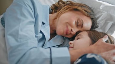 Tembel anne yatak odasının iç tarafında yatıyor. Rahat beyaz yastıklarda sabah ayininin keyfini çıkaran mutlu kız. Pijamalı anne ve kızının huzurlu ve şefkatli ailesi sükuneti hissediyorlar.