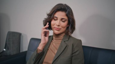 Mutlu yönetici ofis kanepesinden akıllı telefonu arıyor. Rahatlamış şirket içinde gülümseyen iş kadını hoş bir telefon görüşmesi yapıyor. Zarif esmer, konuşan cep telefonu deri koltukta oturuyor..