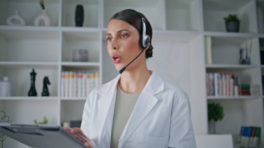 Modern klinikte çağrı ile tedavi öneren kulaklıklı bir doktor. Kadın doktor uzman danışmanlığı yapıyor. Hasta bilgilerini ankete yazıyor. Poliklinikte sağlık görevlisi kulaklıkla konuşuyor..