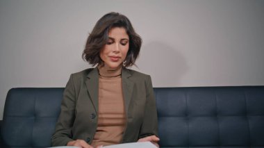 Modern koltukta oturmuş broşürde bilgi okuyan zarif bir bayan. Güzel iş kadını görünümlü moda dergisi ofis koridorunda iş görüşmesi bekliyor. Harika bir kadın kanepenin sayfalarını çeviriyor.