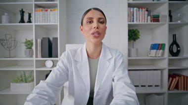 Gülümseyen tıbbi danışman sağlık merkezinde sağlık tavsiyelerini tartışıyor. Uzaktan kumandalı toplantı videosunda dost canlısı kadın doktor danışmanlık yapıyor. Beyaz cüppeli doktor video çağrısına göre konuşuyor..