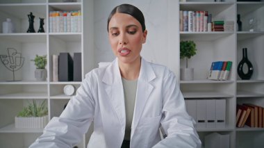 Poliklinikte tedavi tavsiyesi veren online sağlık danışmanı portresi. Kadın doktor uzaktan kumandalı bir video sunuyor. İnternetteki konferansta konuşan olumlu doktor.