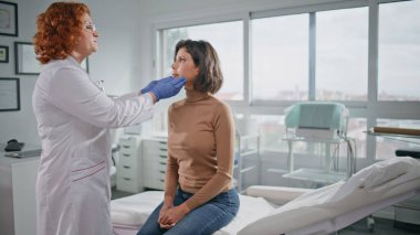 Doctor palpating woman neck in healthcare clinic. Polyclinic specialist making health checkup in medical consultation. Redhead physician examining female throat at medicare visit. Clinical examination clipart