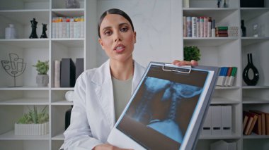 Doktor, klinikteki yakın çekim pov videosunda röntgen görüntülerini sunuyor. İskelet muayenesi için tablet kullanan beyaz önlüklü bir sağlık danışmanı. Kadın radyolog poliklinikte video çağrısında konuşuyor..