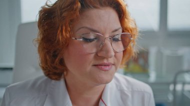 Portre, klinikte kimliği belirsiz bir hastayla konuşurken odaklanmış. Kızıl saçlı sağlık uzmanı, gözlüklü, sağlık hizmetleri uzmanı. Sağlık hizmetleri danışmanlığı yapan bir pratisyen hekim