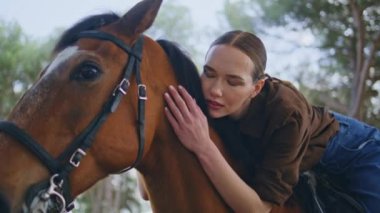 Equestrienne yaz ormanlık alanda at okşayan kafa yakın çekim. Yumuşak bir kadın yemyeşil doğada kahverengi bir hayvanı kucaklıyor. Gülümseyen kadın parkta evcil hayvanla bağ kuruyor. Mutlu kadın nazikçe okşayan aygır