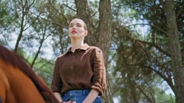 Jockey girl looking distance riding horse at woods closeup. Relaxed confident lady sitting in saddle enjoying horseback strolling at summer nature. Serious proud woman spending time with wild animal