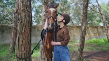 Bayan binici, bahçedeki rahat evde aygır okşuyor. Binicilik eğitiminden önce nazik bir kadın kahverengi ata dokunuyor. Mutlu sahip yeşillik doğasında evcil hayvanla iletişim kurarak sevgisini ifade ediyor. Hobi konsepti 