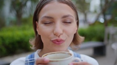 Park terasında kahvesini yudumlayan, çevresi yeşilliklerle çevrili bir kadın. Açık hava kafeteryasında sabah taze espresso içen gülümseyen sakin kızın portresi. Sokakta fincanla poz veren çekici bir model..