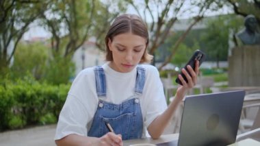 Defterine notlar alan ciddi bir serbest çalışan açık hava kafeteryasında akıllı telefon tutuyor. Bilgisayarda yazı yazan kız öğrenciye odaklanmış. Sokak kafesinde çalışan zeki bir kadın..