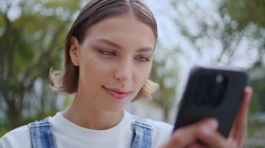 Green Park 'ta cep telefonuna mesaj atan gülümseyen bir kadın. Akıllı telefonların sosyal medya hesaplarına bakan mutlu bir kız. Rahat bayan genç şehir caddesinde cep telefonuyla iletişim kuruyor..