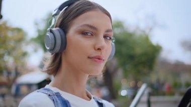Kulaklıkla sokakta poz veren kız cep telefonunu yakın çekimde tutuyor. Şehir parkında telsiz kulaklıkla müzik dinleyen güzel bir kadının portresi. Şık bayan hippi kameralı cep telefonuna bakıyor..
