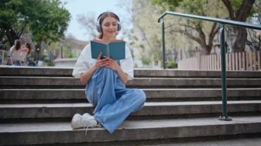Parktaki merdivenlerde kulaklık takarak kitap okumaya odaklanmış moda bir öğrenci. Sakin kız, güneşli gökyüzünün altında entellektüel kovalamacanın tadını çıkarıyor. Kulaklıklı sakin bir genç sokakta roman okuyor..