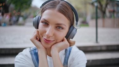 Şehir parkında kablosuz kulaklıkla müzik dinlerken gülümseyen ressam kız. Sokakta beton merdivenlerde oturan rahat ve genç bir kadın. Tasasız genç, kulaklık sesinden hoşlanıyor..