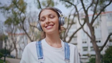 Kulaklıkla müzik dinlemekten hoşlanan mutlu bir kadın şehir parkında yürüyor. Kaygısız bayan hippi, kablosuz kulaklıkla şehir sokaklarında dolaşıyor. Kulaklıklı gülümseyen kız hafta sonu dinleniyor..