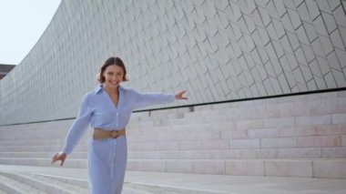 Modern şehir mimarisinin yakınındaki kameraya gülümseyen neşeli bir model. Mutlu bir ifadeyle yakın plan. Şehir merdivenlerinde mavi elbiseyle yürüyen zarif bir esmer. Kasabanın önünde poz veren neşeli kadın.