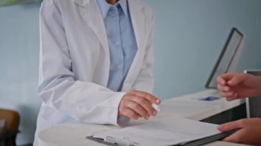 Doktor, sağlık hizmetleri bürosunda belgeleri imzalıyor. Klinikteki muayenede bilinmeyen bir tıbbi uzman evrakları inceliyor. Modern hastanede sigorta formu dolduran kadın pratisyen..